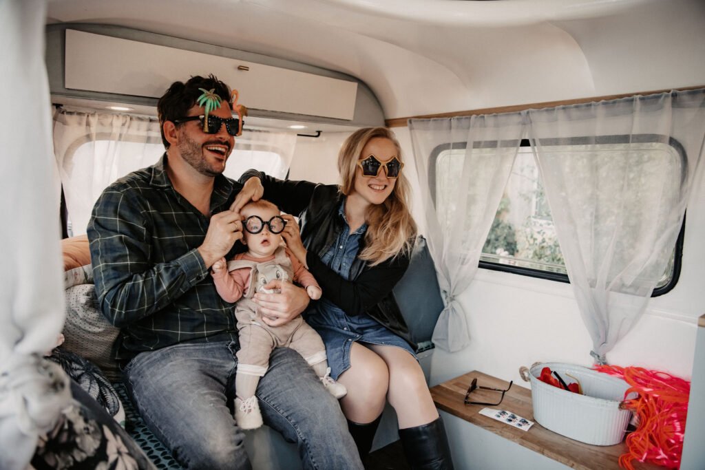 Deux adultes et un enfant portant des lunettes fantaisie, assis à l’intérieur d’une caravane photobooth vintage.